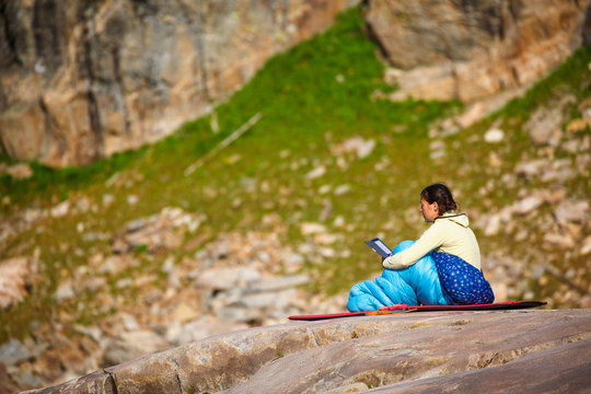 A female backpacker reads from an e-reader at sunset in the Alaska Basin at the edge of the Grand Teton National Park.