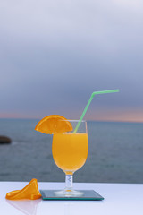 Close-up of a glass with delicious orange juice and two slices of ripe orange and the sea bottom - Fresh and ripe orange