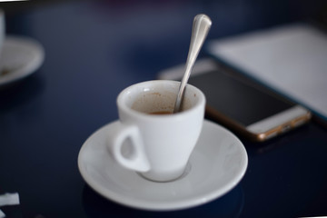 Dark photo of an espresso cup on a blue table accompanied by a cell phone and a notebook - Delicious breakfast