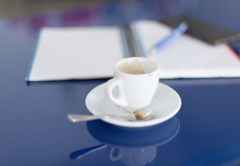 A breakfast coffee on a blue table with a notebook and a cell phone - Coffee mug with selective focus