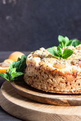 Cheesecake with apricot and crumble, fresh apricots and mint. Wooden background, rustic style. Copy space.