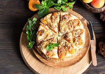 Cheesecake with apricot and crumble, fresh apricots and mint. Wooden background, rustic style. Copy space.