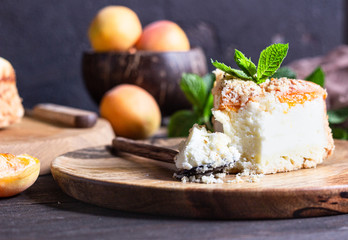 Cheesecake with apricot and crumble, fresh apricots and mint. Wooden background, rustic style. Copy space.