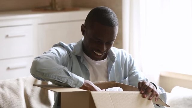 Happy african man customer open parcel cardboard box at home