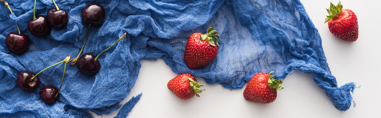 panoramic shot of whole and red strawberries, sweet blueberries on blue cloth