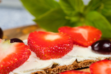 loaves with cheese, strawberries and cherries on a cutting board and gray background with mint leaves