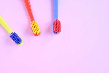Three colorful plastic toothbrush with selective focus on blurred pink background. Multicolored toothbrushes for personal daily healthcare. Toothbrushes for daily oral hygiene and caries protection