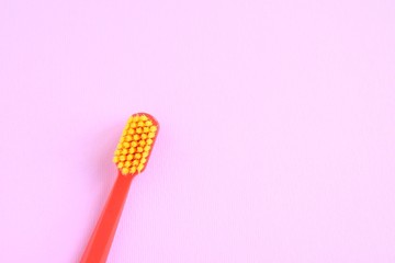 Red plastic toothbrush with bright yellow bristles with selective focus on blurred pink background...