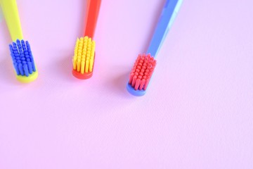 Three colorful plastic toothbrush with selective focus on blurred pink background. Multicolored toothbrushes for personal daily healthcare. Toothbrushes for daily oral hygiene and caries protection