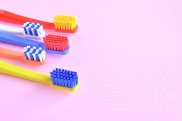 Row of Colorful toothbrushes with selective focus on blurred pink background. Dental tools for daily teeth protection. Multicolored plastic toothbrush with bright bristles with soft focus. Oral hygien