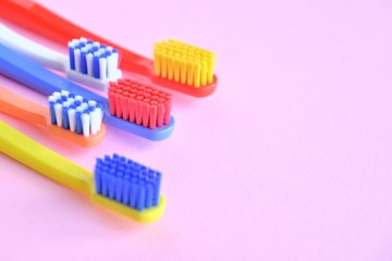 Row of Colorful toothbrushes with selective focus on blurred pink background. Dental tools for daily teeth protection. Multicolored plastic toothbrush with bright bristles with soft focus. Oral hygien