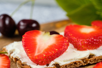 loaves with cheese, strawberries and cherries on a cutting board and gray background with mint leaves