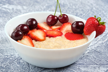 porridge in a white bowl with strawberries and cherries on a gray background