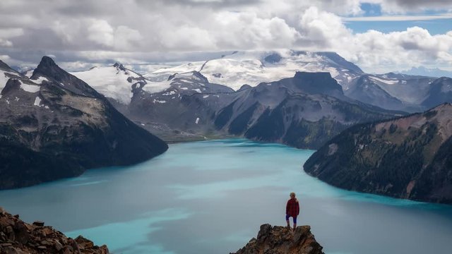 Cinemagraph of Woman standing on top of the Mountain overlooking a beautiful glacier lake. Taken on Panorama Ridge, Garibaldi, Near Whistler, BC, Canada. Still Image Continuous Animation
