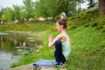 Slender young brunette yogi performs complex yoga exercise on green grass in the summer on a...