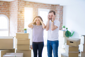 Middle age senior couple moving to a new home with boxes around suffering from headache desperate and stressed because pain and migraine. Hands on head.