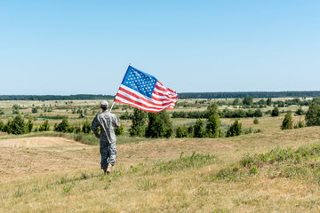 back view of military man holding american flag while walking on grass