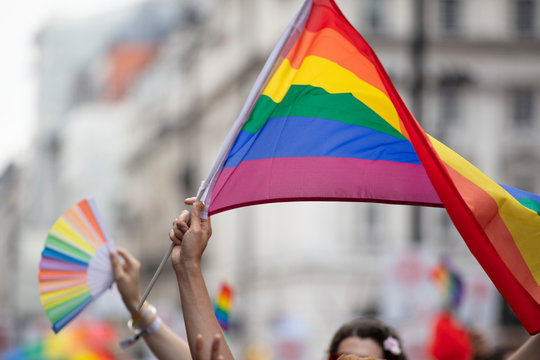 An LGBTQ rainbow flag being waved high in the air at a gay pride march