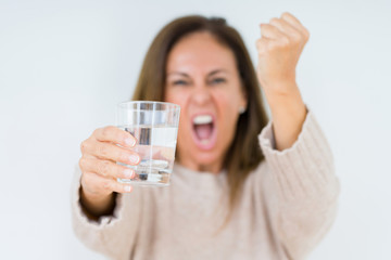 Middle age woman drinking glass of water isolated background annoyed and frustrated shouting with anger, crazy and yelling with raised hand, anger concept