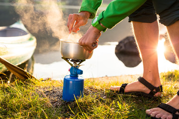 Oppstrynsvatnet Lake, Stryn, Nordfjord, Norway: A man cooking oatmeal by the lake with the rising sun and a canoe in the background.