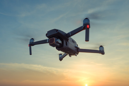 Professional shooting drone flies in the air at low altitude against a blue sky and orange sunset. Drone makes photos. Modern new technology. Ready background with place for your text.