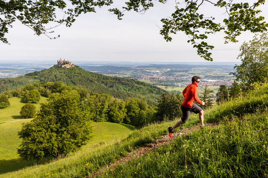 "Traufgang Zollernburg-Panorama" trail, Albstatt-Onstmettingen, Baden-W&cedil;rttemberg, Germany: A male runner running up a steep trail with the Hohenzollern Castle in the background.