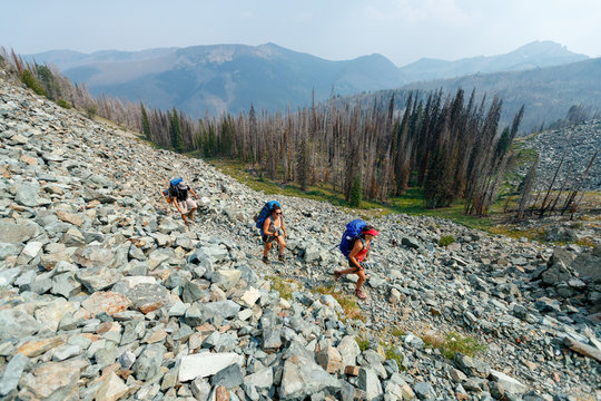 A group of three backpackers hike through old burn areas while the haze from area forest fires obscures the horizon in the Seven Devils Mountains, Idaho.