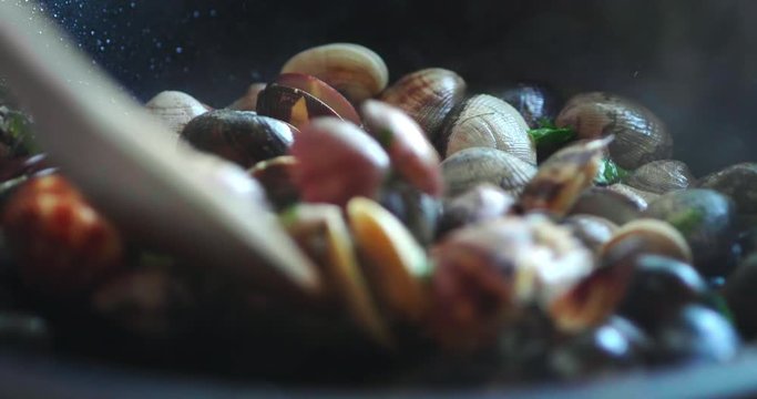 Authentic shot close up of housewife with wooden spoon is mixing the fresh clams during cooking the sauce with parsley for family dinner in the kitchen.