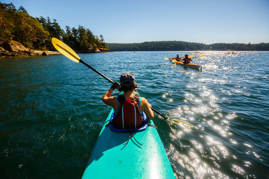 A group of kayakers paddle under blue skies through Wasp Passage near Shaw Island (in the distance) during a 3-day tandem kayaking trip in the San Juan Islands of northwest Washington.