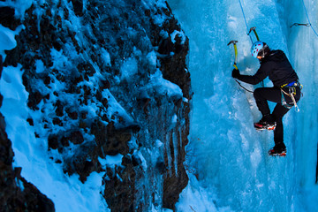 A woman climbs Over Easy (WI3) at Hyalite Canyon in Montana in early evening light.