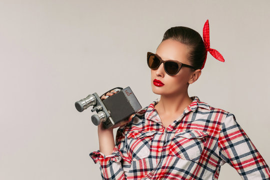 pin-up girl in plaid shirt and sunglasses holding old vintage camera.