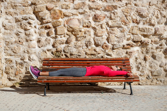 A female runner rests on a bench in the medeival old town section of Cuenca, Spain. The area is a UNESCO World Heritage Site and popular tourist destination.