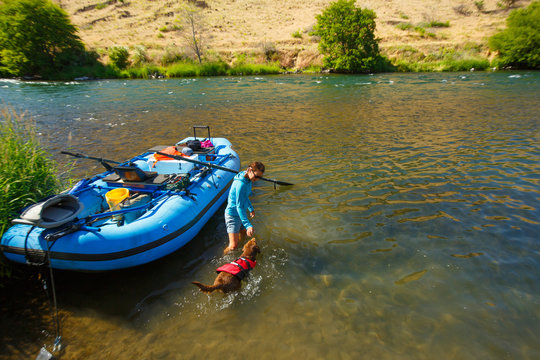 A woman plays with a chocolate lab next to a raft during a float of the Deschutes River in Oregon.