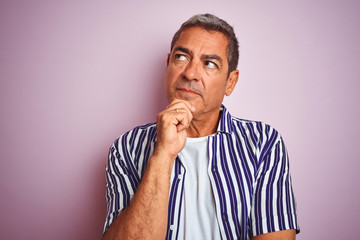 Handsome middle age man wearing striped shirt standing over isolated pink background serious face...