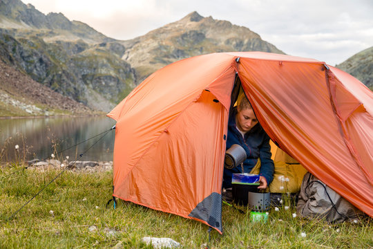 Spronser Lakes Hike, South Tyrol, Italy: A woman preparing instant food from inside her tent at the shore of the "long lake" (Langsee / Lago Lungo), one of the Spronser Lakes.