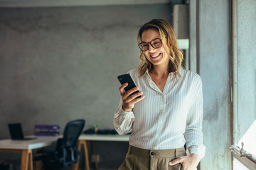 Smiling businesswoman using phone in office - Powered by Adobe