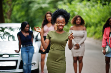 Group of five happy african american girls posed against car, one of them show keys.