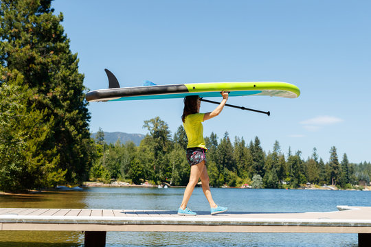 A woman walks down a dock holding  a stand up paddle board in preparation for some SUP at Lake Pend Oreille in northern Idaho.