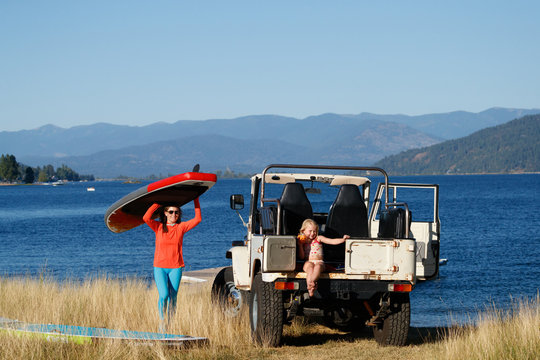 A mother and her daughter prepare to stand up paddle at Lake Pend Oreille next to an old classic FJ Cruiser in the summer.
