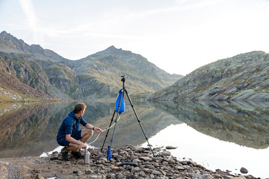 Spronser Lakes Hike, South Tyrol, Italy: A man filtering water at the shore of the "long lake" (Langsee / Lago Lungo), one of the Spronser Lakes.