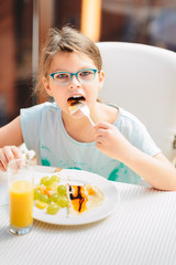 Obraz na płótnie Canvas Cheerful girl eating pancakes, fresh fruits and drinking orange juice during breakfast. Healthy Lifestyle, Vegetarian Diet And Meal
