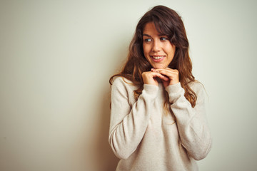 Young beautiful woman wearing winter sweater standing over white isolated background laughing nervous and excited with hands on chin looking to the side