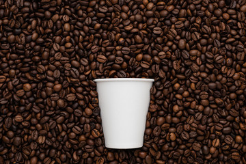 White disposable cup of coffee to go on the background of roasted beans.