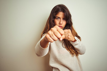 Young beautiful woman wearing winter sweater standing over white isolated background Punching fist to fight, aggressive and angry attack, threat and violence