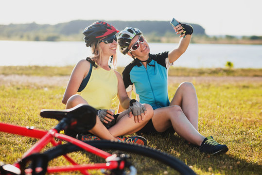 Two friends women wearing cycle gear sitting on grass and take selfie