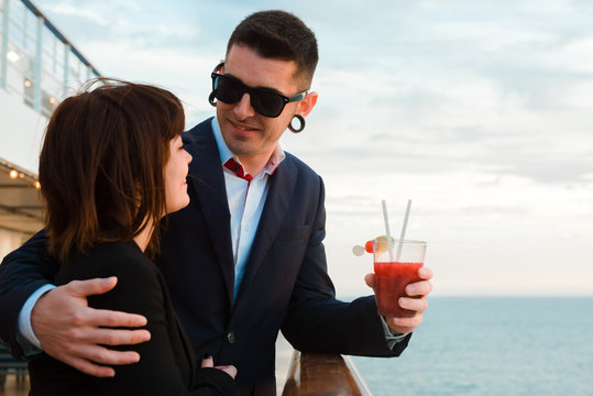 Young attractive couple drinking red beverage with straws from one glass on background of sunset sea