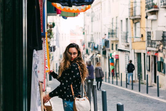 Side view of young woman looking at colorful clothes for sale standing at stall on street of old city