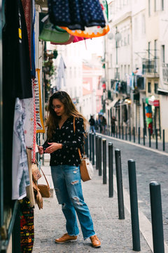 Side view of young woman looking at colorful clothes for sale standing at stall on street of old city