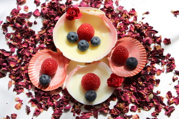 Himbeeren und Blaubeeren arrangiert auf Muscheln und getrockneten Rosenblättern