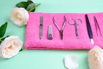 set of tools for manicure on a pink terry towel in the surrounding of pink flowers on a bright background